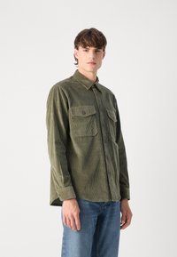 Olijfgroen corduroy overhemd met twee borstzakken, knoopsluiting en een kraag. Heeft een geribbelde textuur en een ontspannen pasvorm.
