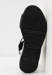 Suola di scarpa in gomma nera con un motivo a strisce ondulate e il logo "GEOX" impresso; presenta una superficie liscia e fori di ventilazione per la traspirabilità.