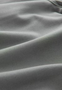 Grau gepolsterter Stoff mit einer glatten Textur, weist subtile Falten und Knicke auf, die auf ein flexibles, leichtes Material hindeuten.