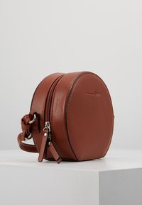 Borsa a mano rotonda in pelle marrone con chiusura a zip, dotata di una piccola tracolla laterale e dettagli in metallo argentato sul cursore della zip. Texture liscia.