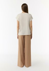 Jasno beżowa bluzka z krótkim rękawem o luźnym kroju, połączona z szerokimi, jasnobeżowymi spodniami w miękkim materiale. Minimalistyczny design, gładka tekstura.