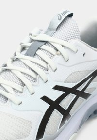 Λευκό και ανοιχτό γκρι αθλητικό παπούτσι με πλέγμα ανάμεσα, υφές, μαύρο σχέδιο λογότυπου και ανακλαστικές λεπτομέρειες στη γλώσσα και τα κορδόνια.