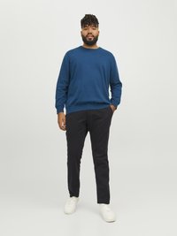 Blå stickad tröja med rund halsringning, ihop med mörka byxor och vita sneakers. Slät textur med ribbade muddar och nederkant.