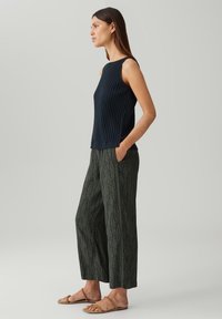 Top senza maniche a costine di colore blu navy abbinato a pantaloni larghi con un motivo a foglie verdi. Sandali piatti completano l'outfit.