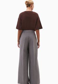 Brązowa, oversize koszulka z krótkim rękawem, w połączeniu z szarymi spodniami o wysokim stanie i szerokich nogawkach, z teksturowanym pionowym prążkowanym wzorem.