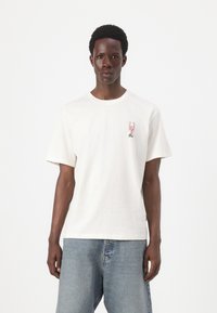 Tricou alb din bumbac, cu mâneci scurte, gât rotund și un grafic mic cu o homar roșu pe piept. Asortat cu blugi din denim de un albastru deschis.