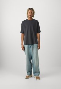 Mørk grå bomulls t-skjorte med rund hals og korte ermer, kombinert med lyseblå vide jeans og brune sneakers med hvite detaljer.