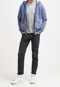 Felpa con cappuccio azzurro chiaro con cerniera, t-shirt grigia, pantaloni scuri e sneakers bianche. Tessuto morbido con vestibilità comoda. Due tasche frontali sulla felpa.