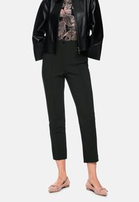 Schwarze Lederjacke, florales Oberteil, hoch taillierte schwarze Hose und rosa Ballerinas mit Schleifendetail. Die Hose hat eine maßgeschneiderte Passform und Nahtakzente.