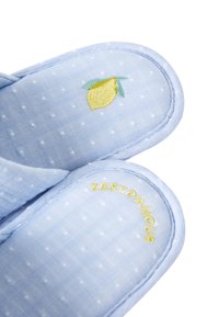 Pantofole in tessuto a pois blu con ricamo di limone e la scritta "ZEST D'AMOUR" in giallo. Design morbido e imbottito, forma rotonda.