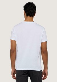 Bílá bavlněná trička s krátkým rukávem, kulatým výstřihem a volným střihem. Viditelné švy a hladká textura.