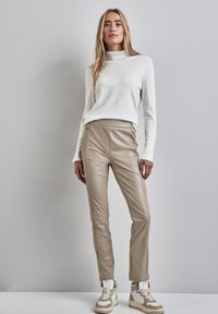 Beige faux leren broek met zijnaad, hoge taille, gecombineerd met een witte lange mouw top en beige hoge sneakers.