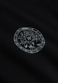 Tissu noir présentant un graphique circulaire détaillé en argent d'un arbre avec des oiseaux et une maison, avec un "W" stylisé au centre.