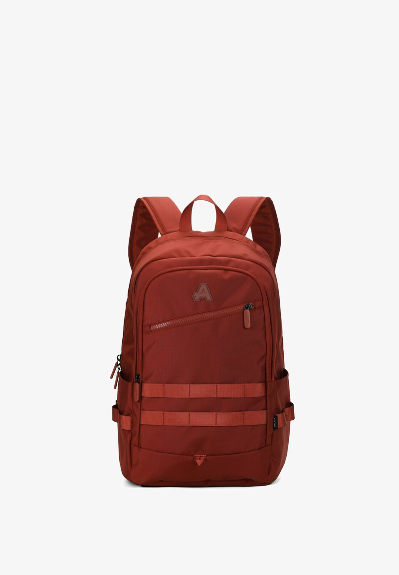 Sac à dos de couleur rouille avec bretelles rembourrées, poche avant zippée en diagonale, doubles sangles horizontales et poches latérales, isolé sur fond blanc.