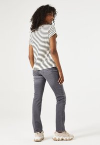 Camiseta de rayas en color crema y negro, corte relajado, combinada con jeans grises ajustados y zapatillas beige gruesas. Cabello rizado peinado de forma natural.