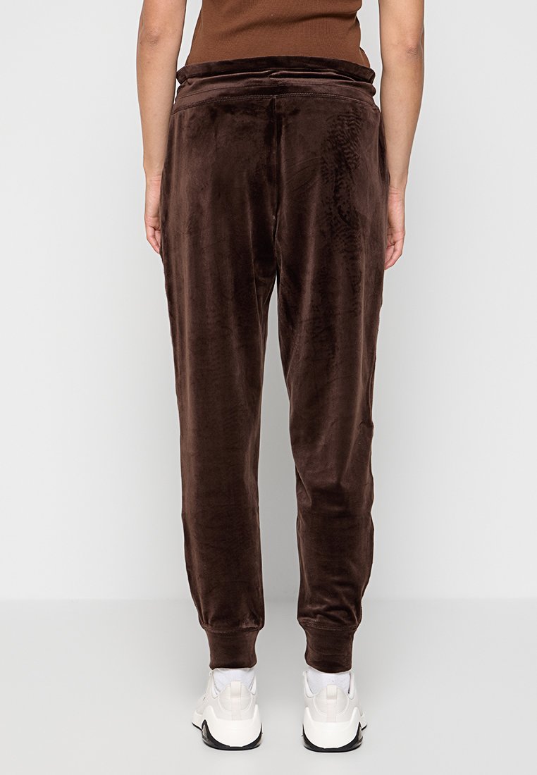 Brązowe dresy z weluru o miękkiej teksturze, zwężane nogawki i elastyczny pas. Połączone z białymi sneakersami, widok z tyłu.