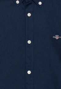 Granatowa koszula zapinana na guziki wykonana z teksturowanej tkaniny, z białymi guzikami i małym haftowanym logo na lewej piersi.