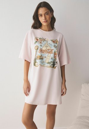 Kvinde iført en lyserød oversized T-shirtkjole med farverigt vintage Coca-Cola kort og blomsterprint foran.