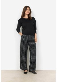 Top nero a maniche lunghe abbinato a pantaloni neri a gamba larga con pois bianchi. Tessuto morbido con vestibilità rilassata e minimalismo nei dettagli.