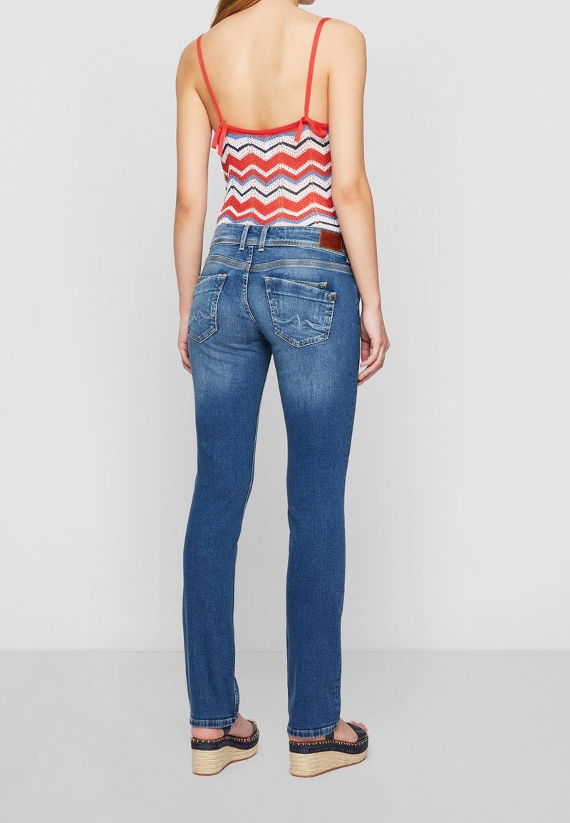 Smala jeans i mörkblå denim med medelhög midja, bakfickor och subtila blekningar. Bärs med en flerfärgad zigzag-top.