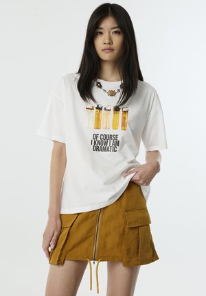 Witte t-shirt met kleurrijke aanstekergraphics en de tekst "Natuurlijk weet ik dat ik dramatisch ben." Gecombineerd met een mosterdgele ritsrok.