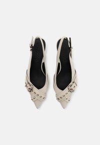 Beige slingback-pumps med spetsiga tår, justerbar spänne och nitar, med en svart innersula med präglad logotyp.