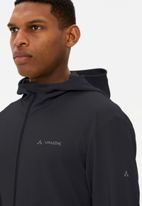 Giacca nera con cappuccio realizzata in tessuto testurizzato. Presenta una chiusura a zip e un discreto logo sul petto e sulla manica.