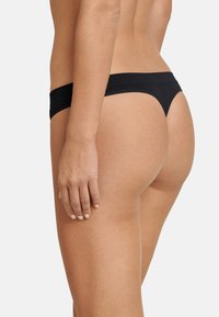 Schwarze Tanga-Unterwäsche aus weichem, elastischem Material; verfügt über ein minimalistisches Design mit einem dünnen Bund und minimaler Bedeckung.