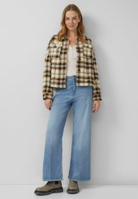 Koszula-jacket w kratę w odcieniach kremu, brązu i czerni; zestawiona z jasnoniebieskimi wysokim stanem szerokimi spodniami jeansowymi i szarymi botkami na kostkę.