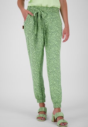 Pantalon vert à motif floral avec poignets élastiques, taille nouée, porté avec des sandales à talons vertes assorties à smocks.