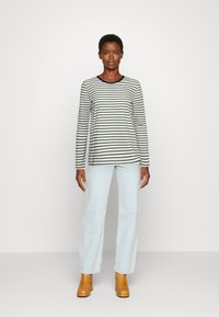 Camisa de manga comprida listrada em creme e azul marinho, com decote redondo, combinada com jeans de perna reta em azul claro e botas de tornozelo em tom castanho.