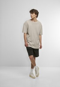 tricou oversized de culoare bej deschis cu mâneci scurte, asociat cu pantaloni scurți negri și adidași bej. Textură netedă, design simplu.