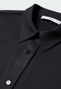 Schwarzes Hemd mit spitzem Kragen, Knopfverschluss mit schwarzem Knopf und glattem, elegantem Gewebe. Etikett sichtbar im Kragen.