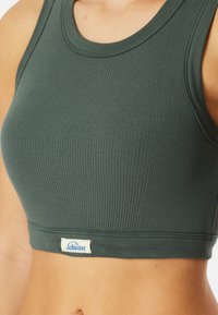 Tmavě zelený žebrovaný crop top s kulatým výstřihem. Disponuje výraznou značkovou etiketou na lemu. Vyrobeno z měkkého a pružného materiálu.