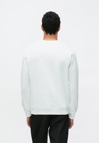 Světle šedá mikina s kulatým výstřihem, dlouhými rukávy a žebrovanými manžetami. Látka má hladkou strukturu a minimální švy.