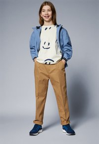 Ljusblå bomberjacka, krämfärgad t-shirt med svarta smiley-ansikten, beige byxor och blå sneakers. Enkelt mönster, avslappnad passform och avslappnad stil.
