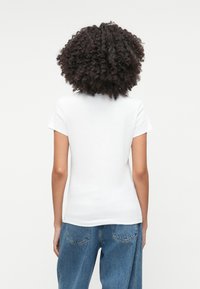 Valkoinen puuvillapaita, jossa on lyhyet hihat ja pyöreä kaula-aukko, yhdistettynä vaaleansiniin farkkuihin. Yksinkertainen, klassinen muotoilu ilman näkyviä kuvioita.