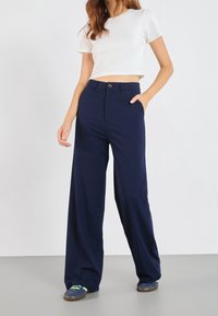 Navy blue wide-leg pants made of lightweight fabric with a front button closure and side pockets, paired with a white cropped top.