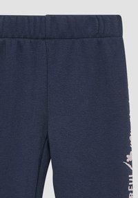 Navyblauwe katoenen joggingbroek met een elastische tailleband, voorzien van een bloemenpatroon in lichtroze op het onderste deel van het rechterbeen.