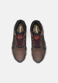 Brown and black athletic shoes with fabric upper, textured panels, contrasting red laces, and rubber outsole. Timberland logo on insole.