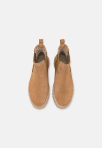 Ciemnobrązowe zamszowe buty typu slip-on z elastycznymi bocznymi panelami, miękką wyściółką wewnętrzną oraz teksturowanymi gumowymi podeszwami. Okrągły nos i subtelne detale.