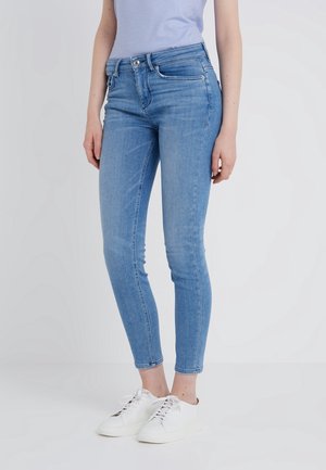 Jeans ajustados de color azul claro hechos de denim, con una cintura de altura media, cinco bolsillos y un sutil efecto de decoloración, combinados con zapatillas blancas.
