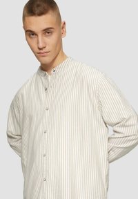 Lichtgewicht gestreept overhemd in beige en wit met een mandarijnkraag en lange mouwen. Voorzien van knopen aan de voorkant en een comfortabele pasvorm.