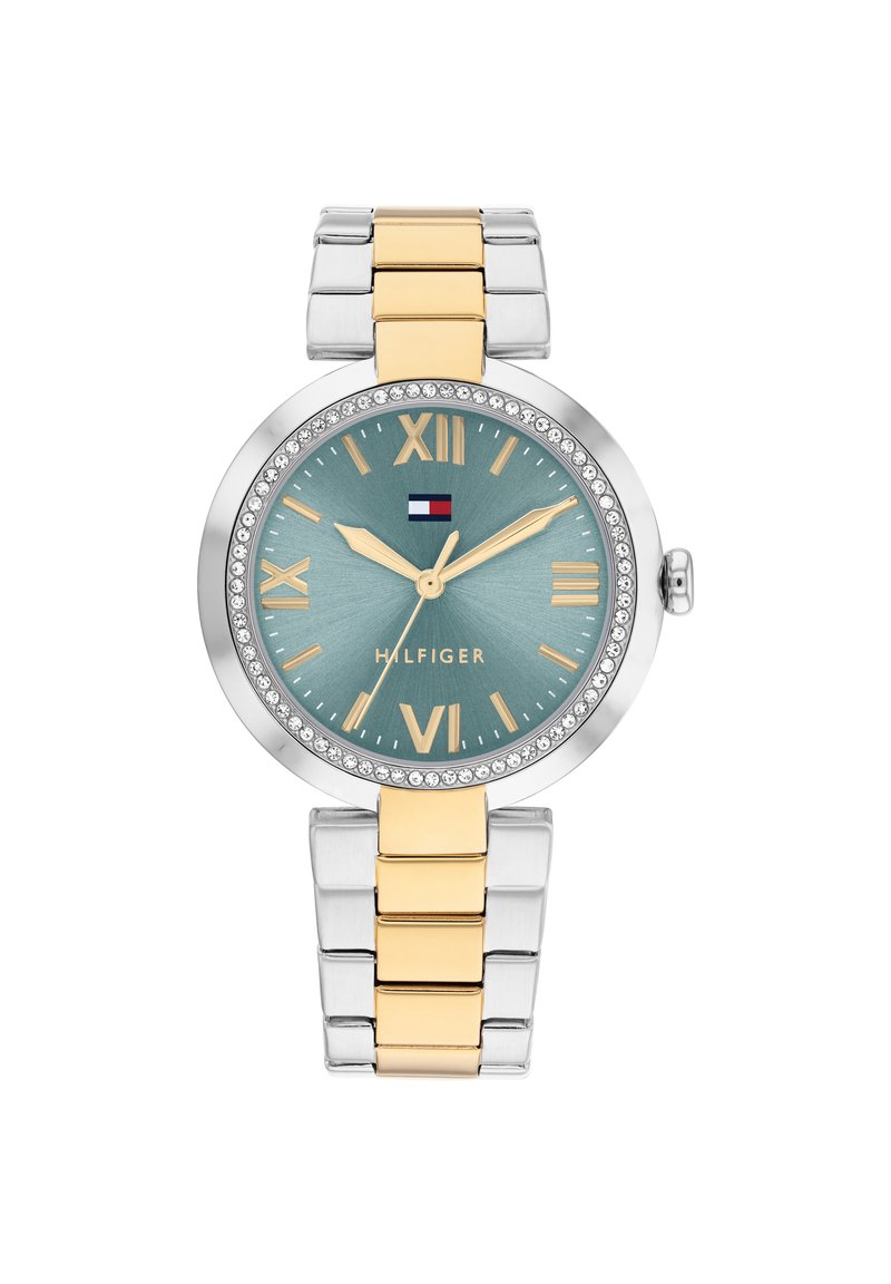 Reloj en tonos plateado y dorado con una esfera redonda, dial en color aqua, números romanos y embellishments de cristal alrededor del bisel. Presenta una pulsera con eslabones.