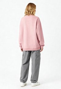 Felpa oversized rosa con maniche lunghe, polsini e orlo a coste. Abbinata a pantaloni cargo grigi dal taglio comodo, dotati di tasche laterali.