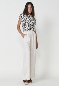 Camisa a rayas en blanco y negro con mangas cortas, combinada con pantalones anchos de color beige claro. Los pantalones tienen una cinturilla elástica y bolsillos.