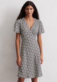 Kurzärmliges Kleid in einem Schwarz-Weiß-Blumenmuster, mit tiefem V-Ausschnitt, tailliertem Schnitt und ausgestelltem Rock. Weicher Stoff.