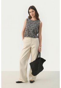 Top senza maniche a motivi bianco e nero, pantaloni beige a gamba larga, scarpe basse nere e borsa a tracolla intrecciata nera. Texture lisce.