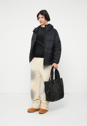 Czarna kurtka puchowa z kapturem, teksturowana tkanina i przednia kieszeń; oversize'owe jasne spodnie z ciemnym gradientem; czarna torba na ramię z uchwytami.