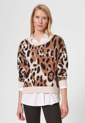 Leopardenmuster-Pullover in Brauntönen, Creme und Schwarz; gestrickte Textur mit gerippten Bündchen und Saum. Über einem weißen Shirt getragen.